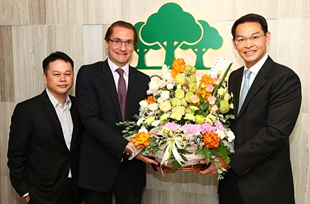 Hubert Viriot, center, Chief Executive Officer of Raimon Land PLC, and Chief Operating Officer Kitti Tungsriwong, left, receive a congratulatory bouquet from Chanitr Charnchainarong, right, the Executive Vice President of the Issuer & Listing Division of the Stock Exchange of Thailand (SET).